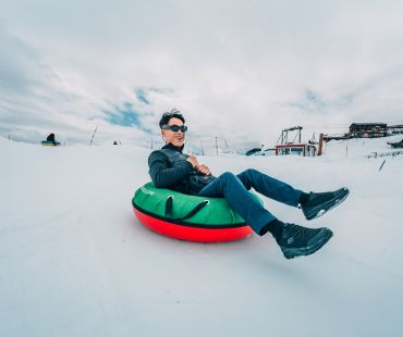 Person enjoying riding snow tube down trails Person enjoying riding snow tube down trails